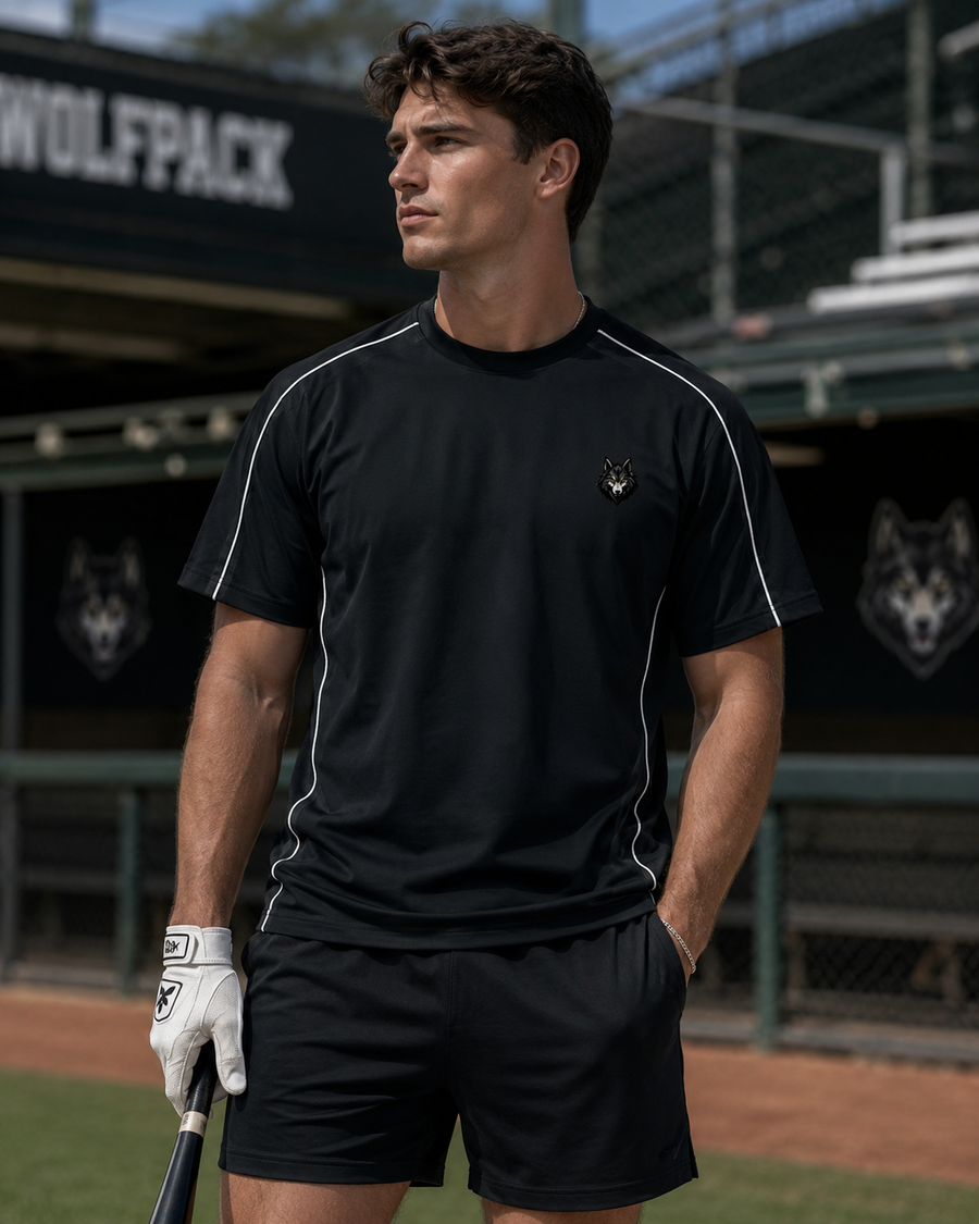 Man in beige athletic wear with visible tattoos, standing outdoors near metal fence.